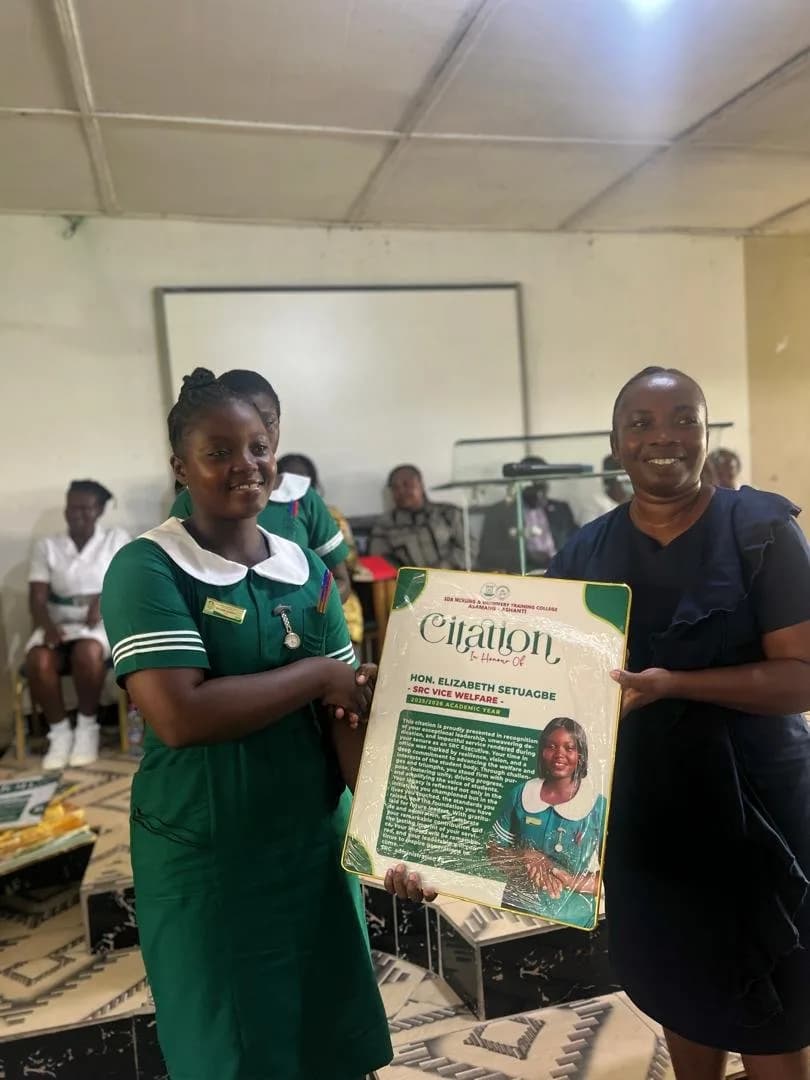 Female student in green nursing uniform presenting citation award to woman in dark dress during handover ceremony