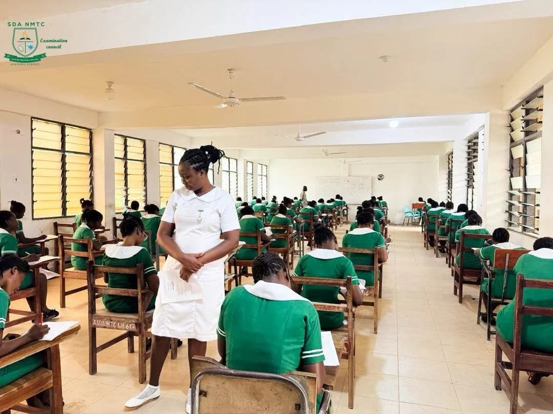 Nursing students in green uniforms taking an exam with a white-uniformed invigilator present