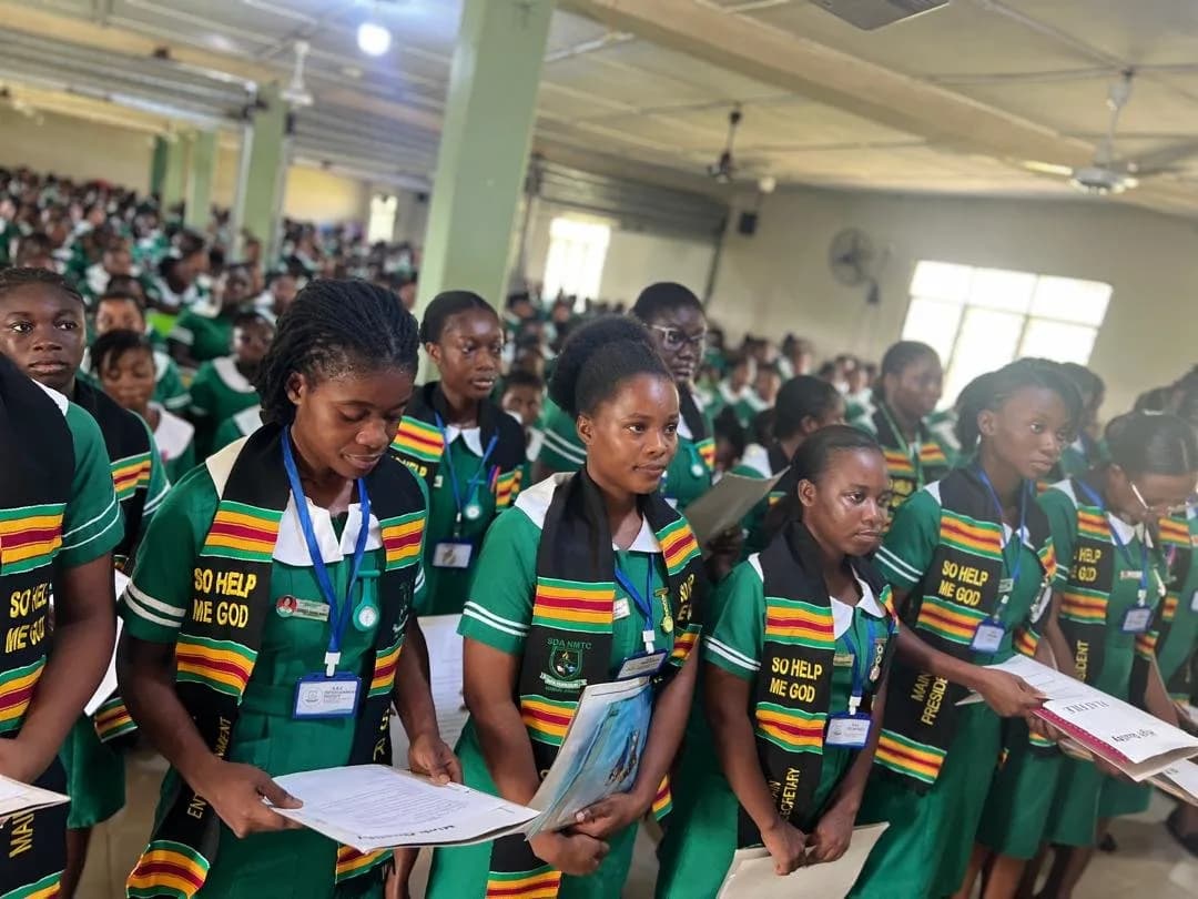 Large assembly of students in green nursing uniforms with colorful scarves seated in auditorium during handover ceremony