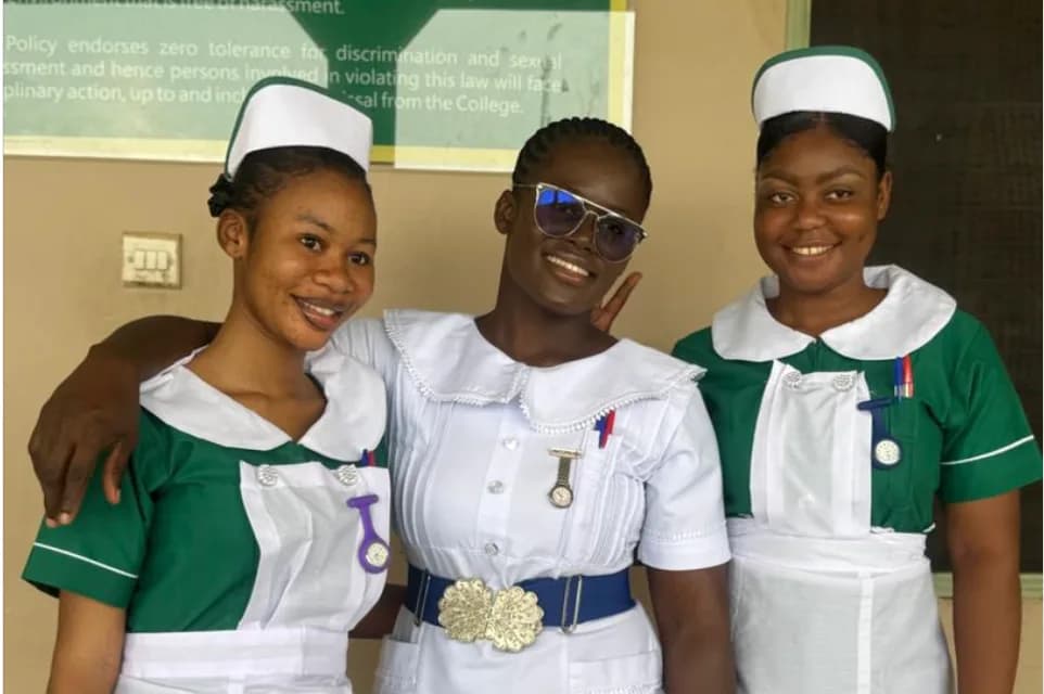 Three nursing students in green and white uniforms smiling at camera in front of anti-sexual harassment policy statement