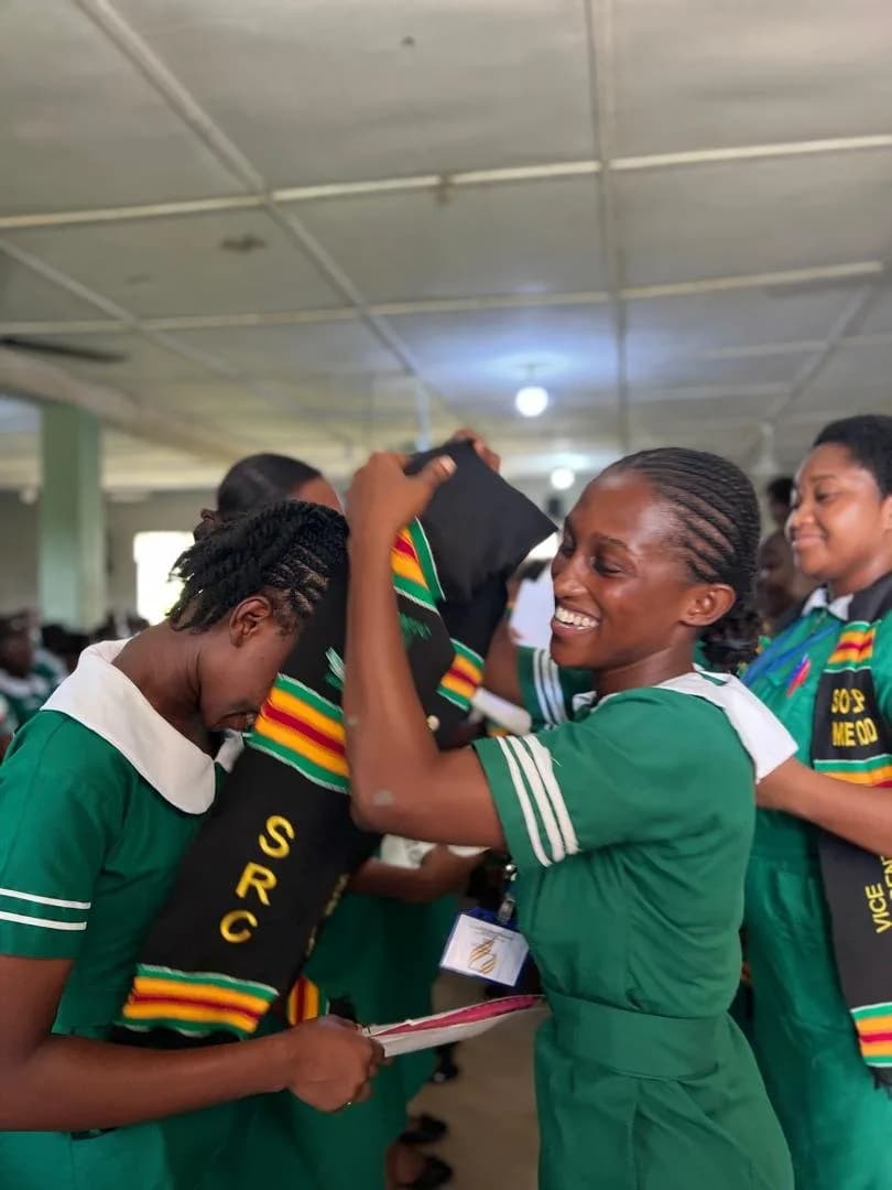 Female students in green nursing uniforms with colorful scarves interacting and celebrating during handover ceremony
