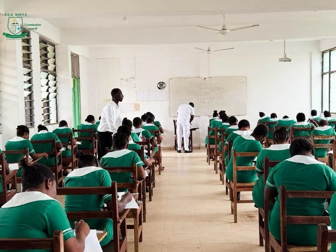 Wide view of examination hall with nursing students in green uniforms supervised by invigilators