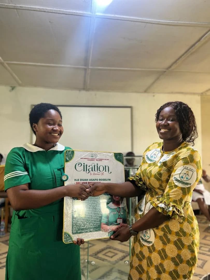 Two female students in green nursing uniform and gold patterned dress presenting citation award during handover ceremony