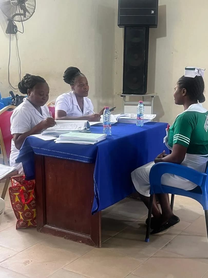 Two examiners reviewing documents while questioning a seated student nurse during the viva
