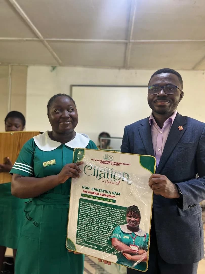 Female student in green nursing uniform presenting citation award to male administrator in blue suit during handover ceremony