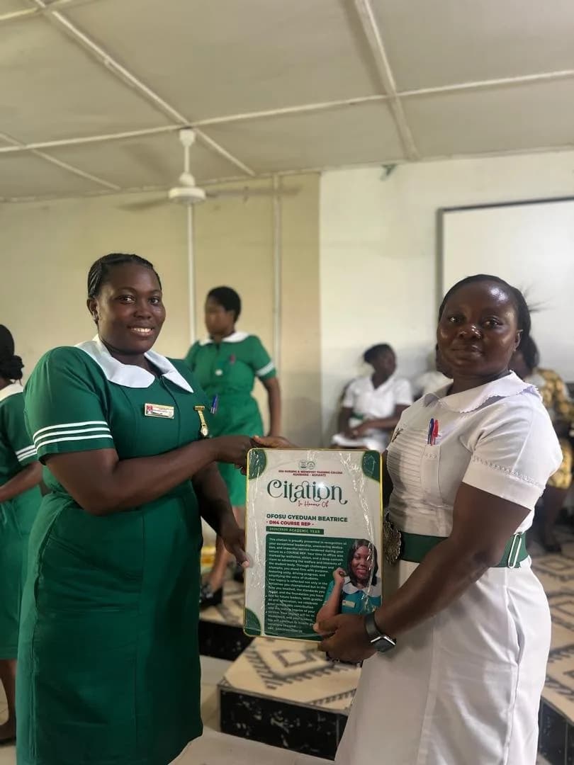 Female student in green nursing uniform presenting citation award to man in white shirt during handover ceremony