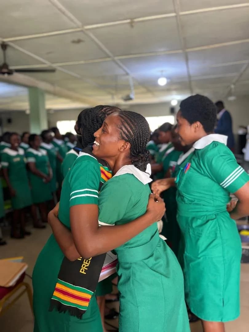 Group of female students in green nursing uniforms with colorful scarves holding documents during handover ceremony