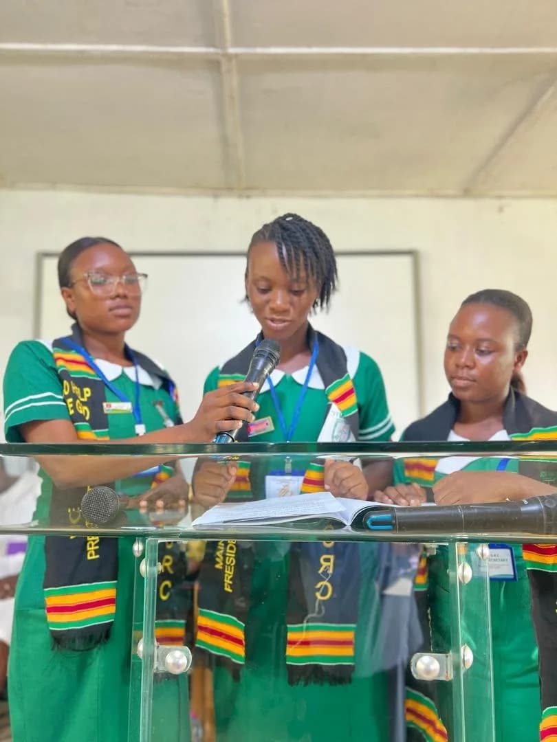 Three female students at podium during SRC handover ceremony with microphones and colorful scarves